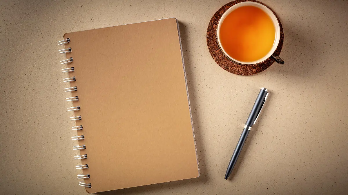 A diary on a desk, shot from above with a pen and a cup of tea on a rustic background