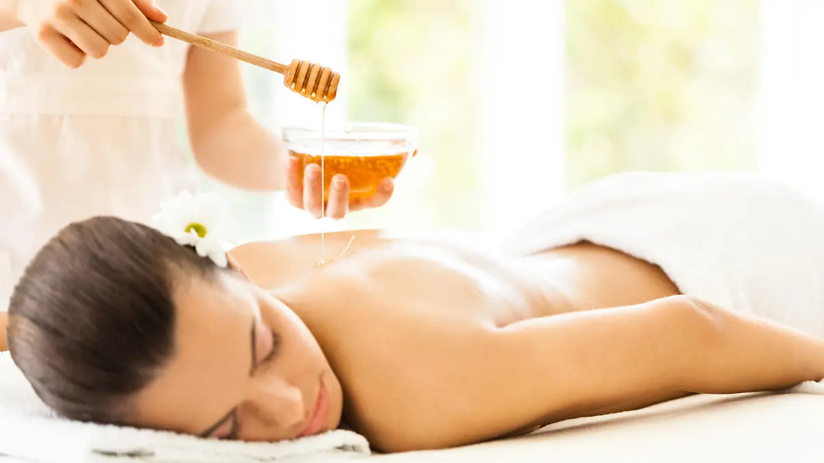 Masseuse pouring honey on woman's back