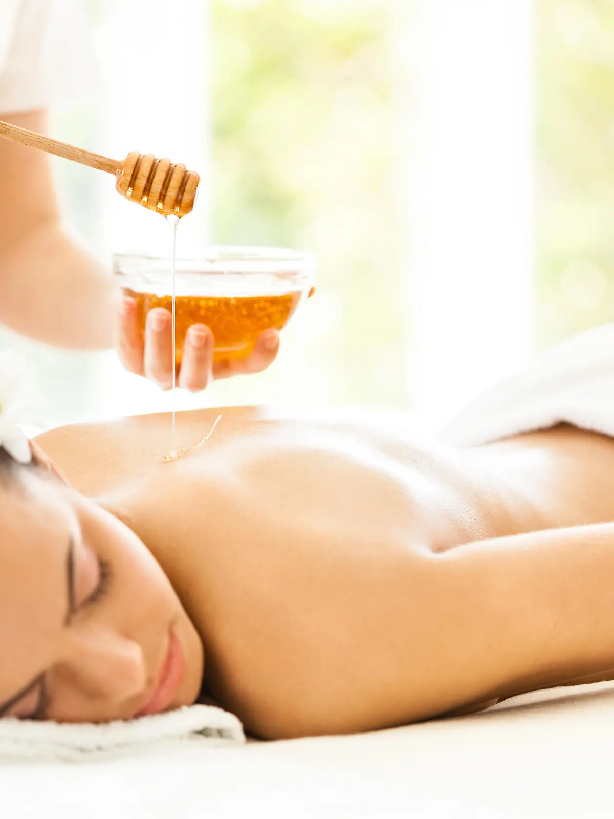 Masseuse pouring honey on woman's back