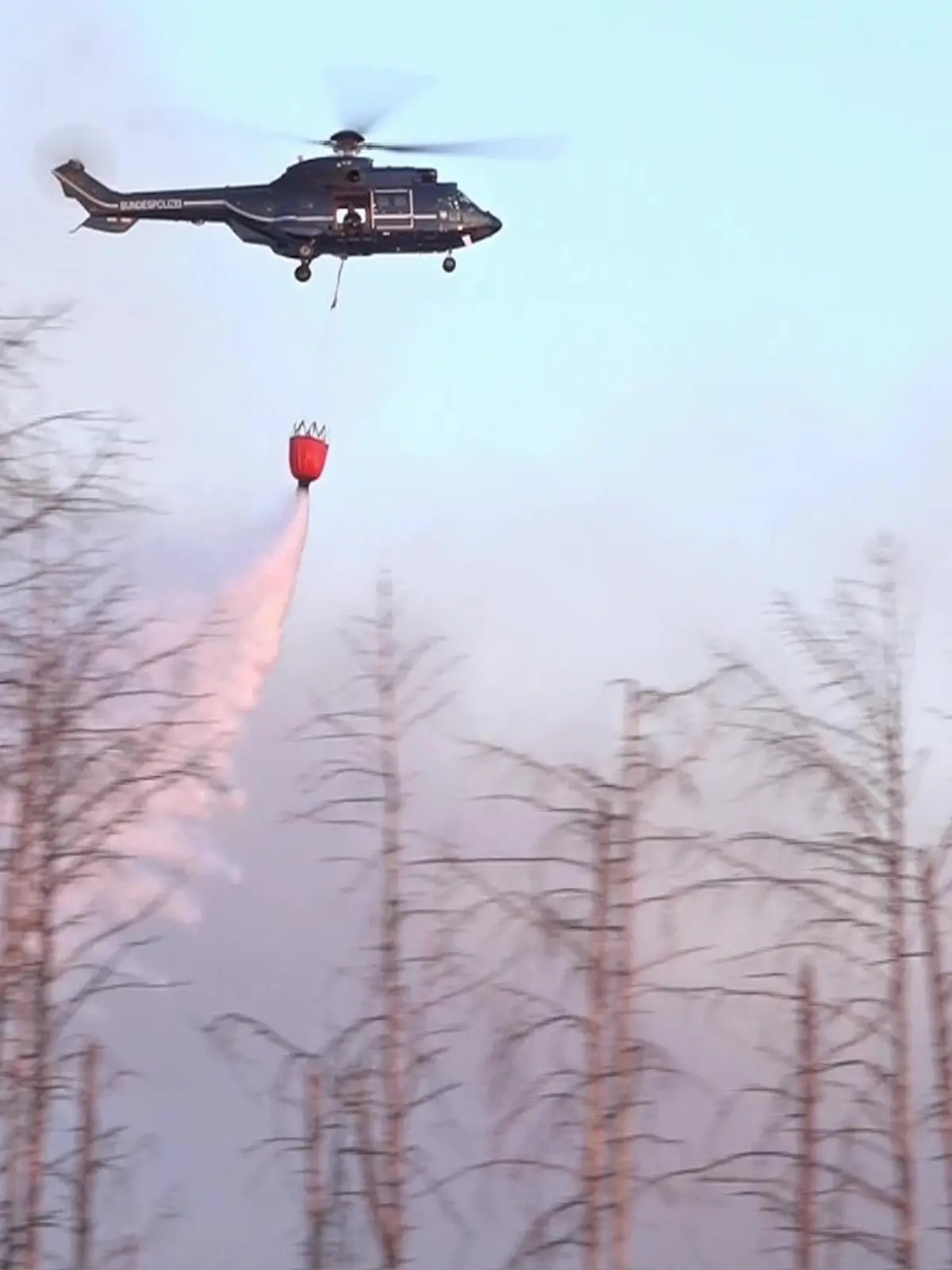 dpatopbilder - 01.06.2023, Brandenburg, Jüterbog: Ein Löschhubschrauber wirft Wasser ab über einem Waldbrand in einem munitionsbelasteten Gebiet bei Jüterbog (Landkreis Teltow-Fläming). Der Waldbrand hat sich trotz des Löscheinsatzes aus der Luft auf rund 27 Hektar ausgebreitet. Foto: Cevin Dettlaff/dpa +++ dpa-Bildfunk +++