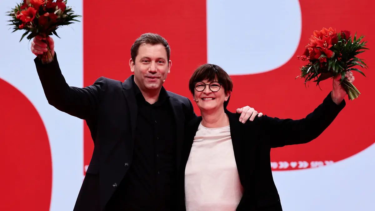 New-elected SPD co-leader Lars Klingbeil, left, poses with re-elected SPD co-leader Saskia Esken, right, as they hold flowers during a hybrid party congress of Germany's Social Democratic Party (SPD) in Berlin, Germany, Dec. 11, 2021. (Hannibal Hanschke/Pool Photo via AP)
