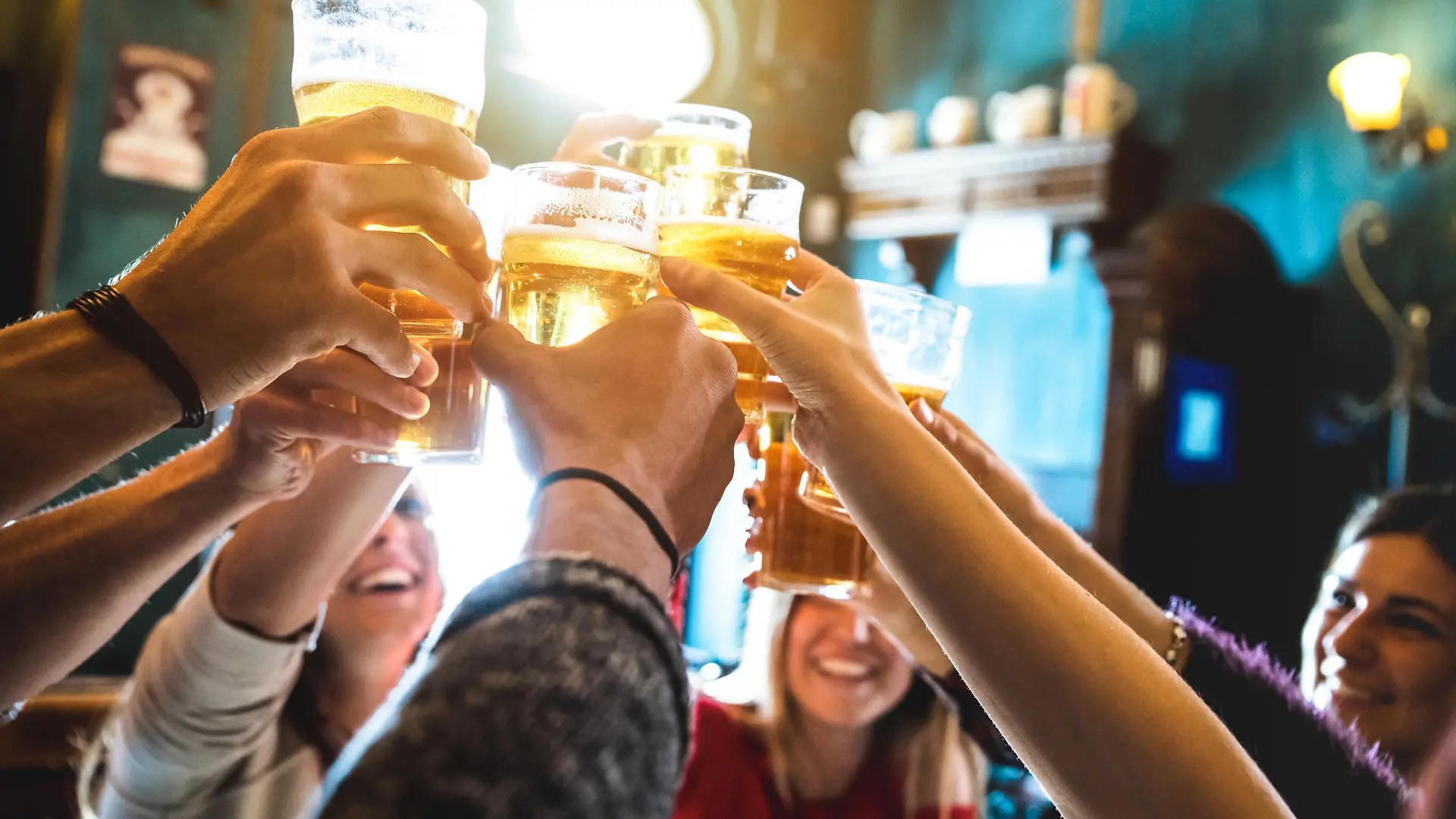 Group of happy friends drinking and toasting beer at brewery bar restaurant - Friendship concept with young people having fun together at cool vintage pub - Focus on middle pint glass - High iso image