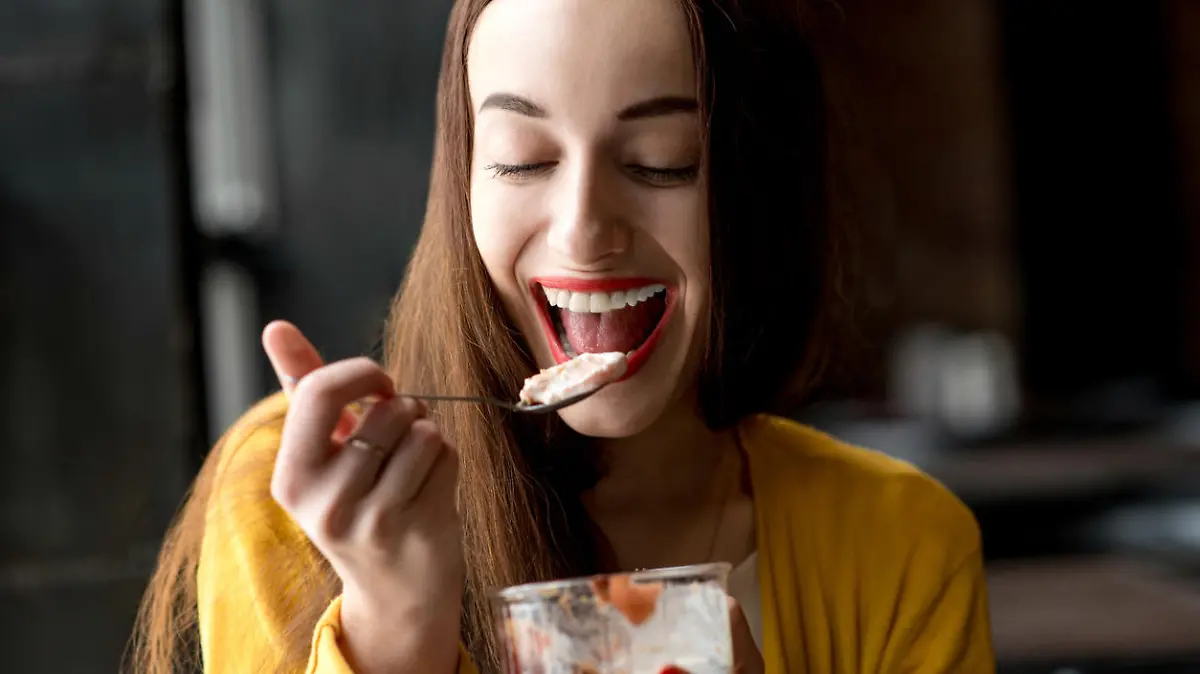 Young smiling woman dressed in yellow sweater eating ice cream in the dark cafe interior