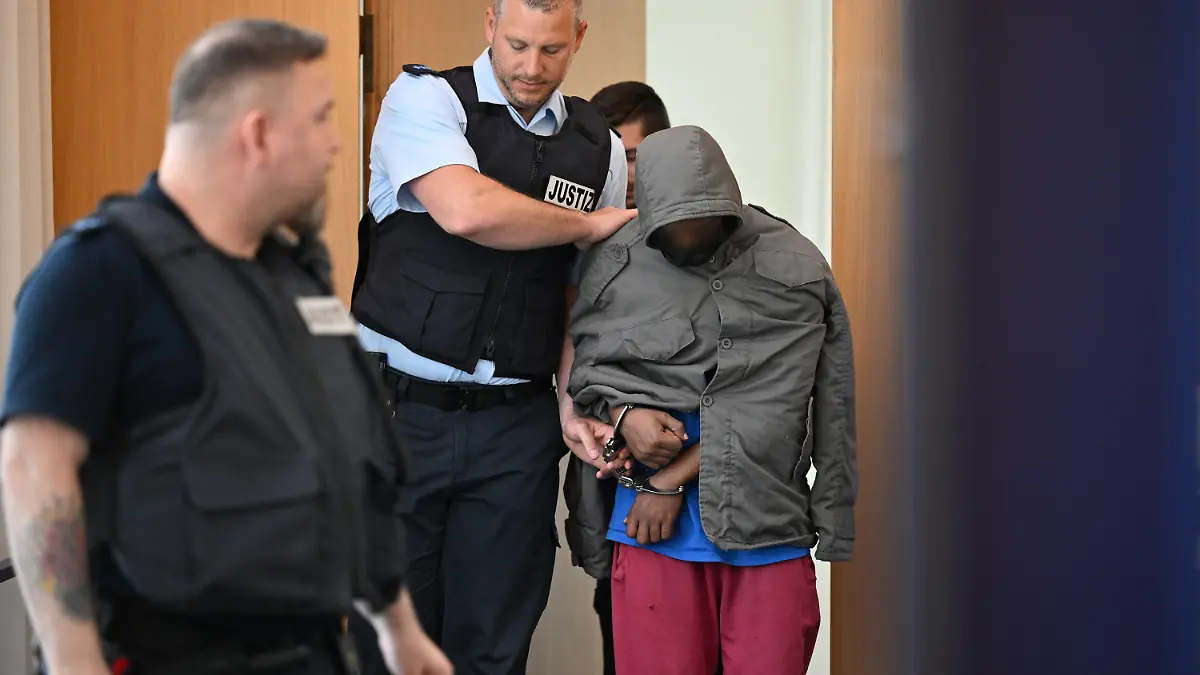 02.06.2023, Baden-Württemberg, Ulm: Der Angeklagte wird in Hand- und Fußschellen in den Gerichtssaal geführt. Der Asylbewerber aus Eritrea soll am 5. Dezember in Illerkirchberg eine 14-Jährige und ihre 13 Jahre alte Freundin auf dem Schulweg mit einem Messer heimtückisch attackiert haben. Die 14-Jährige starb an ihren Verletzungen. Angeklagt ist er wegen Mordes und versuchten Mordes mit gefährlicher Körperverletzung. Foto: Felix Kästle/dpa - ACHTUNG: Person wurde aus rechtlichen Gründen gepixelt +++ dpa-Bildfunk +++