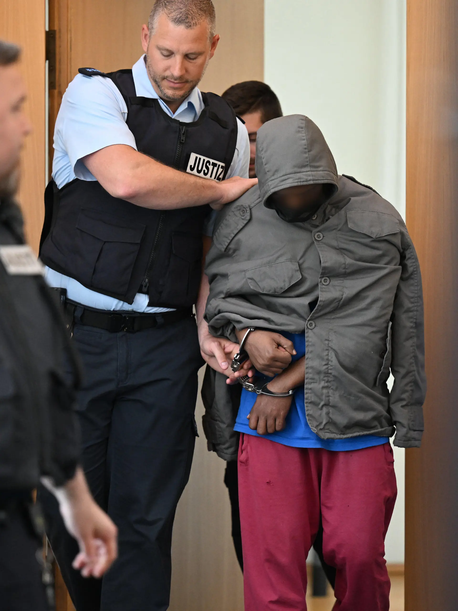 02.06.2023, Baden-Württemberg, Ulm: Der Angeklagte wird in Hand- und Fußschellen in den Gerichtssaal geführt. Der Asylbewerber aus Eritrea soll am 5. Dezember in Illerkirchberg eine 14-Jährige und ihre 13 Jahre alte Freundin auf dem Schulweg mit einem Messer heimtückisch attackiert haben. Die 14-Jährige starb an ihren Verletzungen. Angeklagt ist er wegen Mordes und versuchten Mordes mit gefährlicher Körperverletzung. Foto: Felix Kästle/dpa - ACHTUNG: Person wurde aus rechtlichen Gründen gepixelt +++ dpa-Bildfunk +++