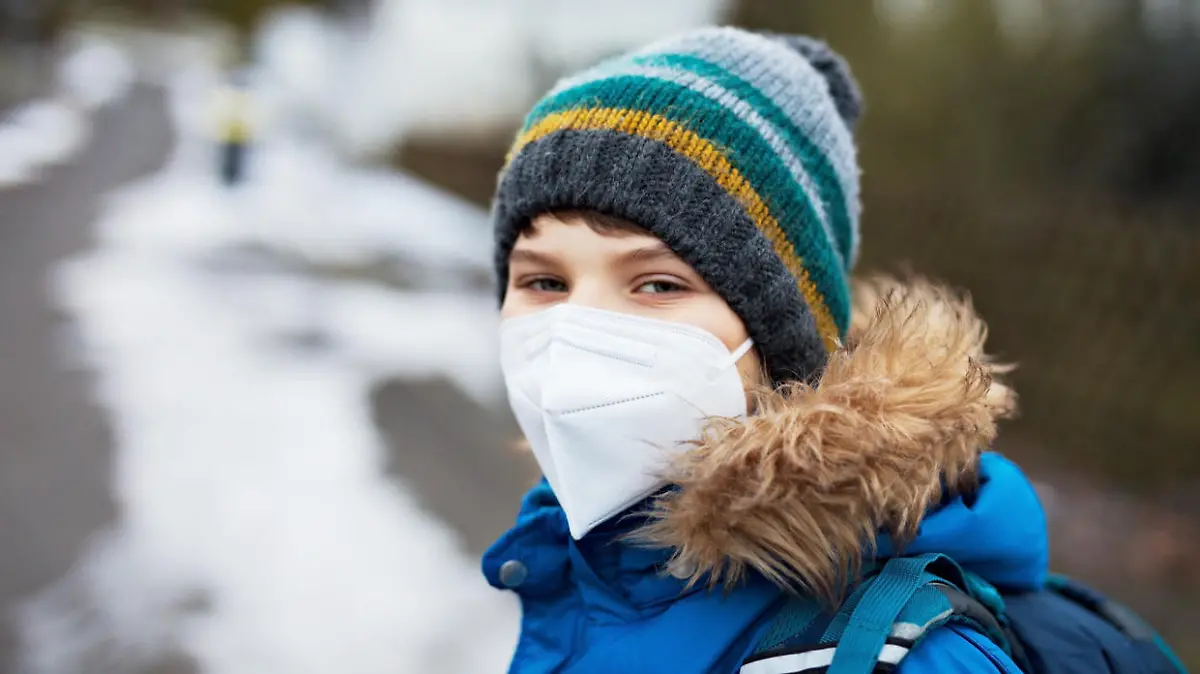 Kid boy wearing ffp medical mask on the way to school. Child backpack satchel. Schoolkid on cold autumn or winter day with warm clothes. Lockdown and quarantine time during corona pandemic disease.