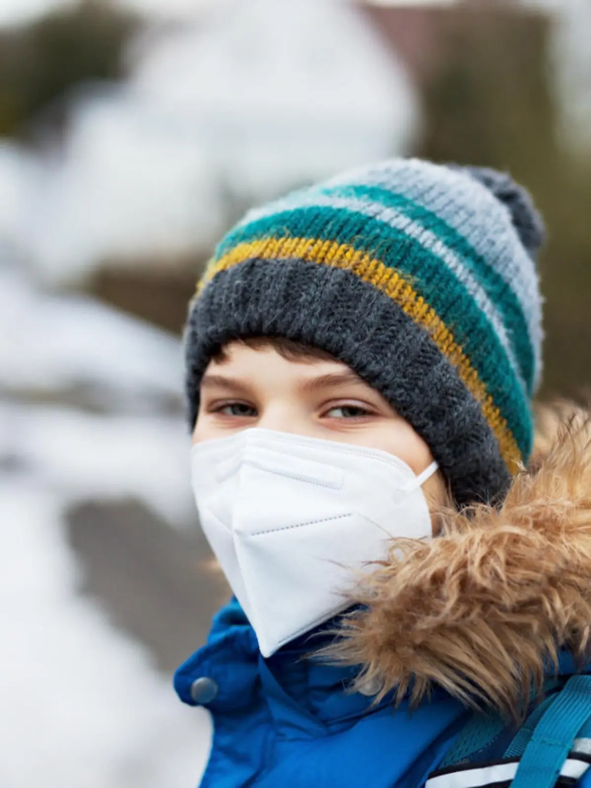 Kid boy wearing ffp medical mask on the way to school. Child backpack satchel. Schoolkid on cold autumn or winter day with warm clothes. Lockdown and quarantine time during corona pandemic disease.