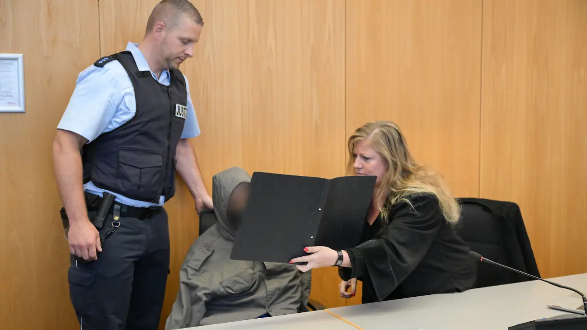 02.06.2023, Baden-Württemberg, Ulm: Der Angeklagte (M) sitzt im Gerichtssaal, während seine Anwältin Corinna Nagel (r) ihm eine Mappe vors Gesicht hält. Der Asylbewerber aus Eritrea soll am 5. Dezember in Illerkirchberg eine 14-Jährige und ihre 13 Jahre alte Freundin auf dem Schulweg mit einem Messer heimtückisch attackiert haben. Die 14-Jährige starb an ihren Verletzungen. Angeklagt ist er wegen Mordes und versuchten Mordes mit gefährlicher Körperverletzung. Foto: Felix Kästle/dpa - ACHTUNG: Person wurde aus rechtlichen Gründen gepixelt +++ dpa-Bildfunk +++