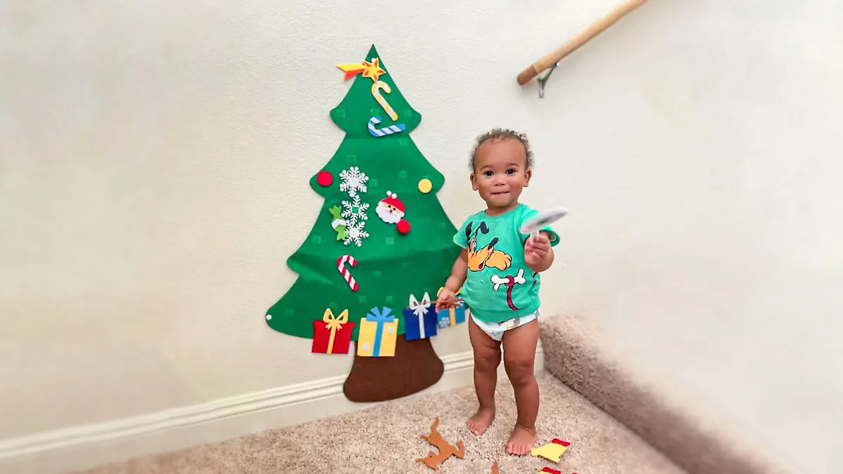 Baby steht neben einem Weihnachtsbaum