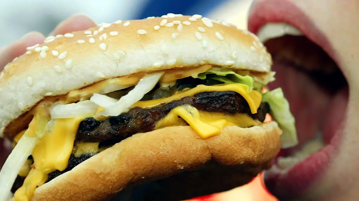 ARCHIV - Eine junge Frau isst am 23.01.2003 in Düsseldorf einen Hamburger. Das höchste Gremium der Weltgesundheitsorganisation (WHO) berät bis zum 24. Mai unter anderem über Maßnahmen gegen die Ausbreitung nicht übertragbarer Krankheiten wie Diabetes, Krebs, Herzleiden oder Fettsucht.  Viele solcher Krankheiten werden durch ungesunde Ernährung begünstigt oder hervorgerufen.   Foto: Gero Breloer/dpa   (zu dpa "UN-Beauftragter regt Konvention gegen ungesunde Ernährung an" vom 19.05.2014) +++(c) dpa - Bildfunk+++