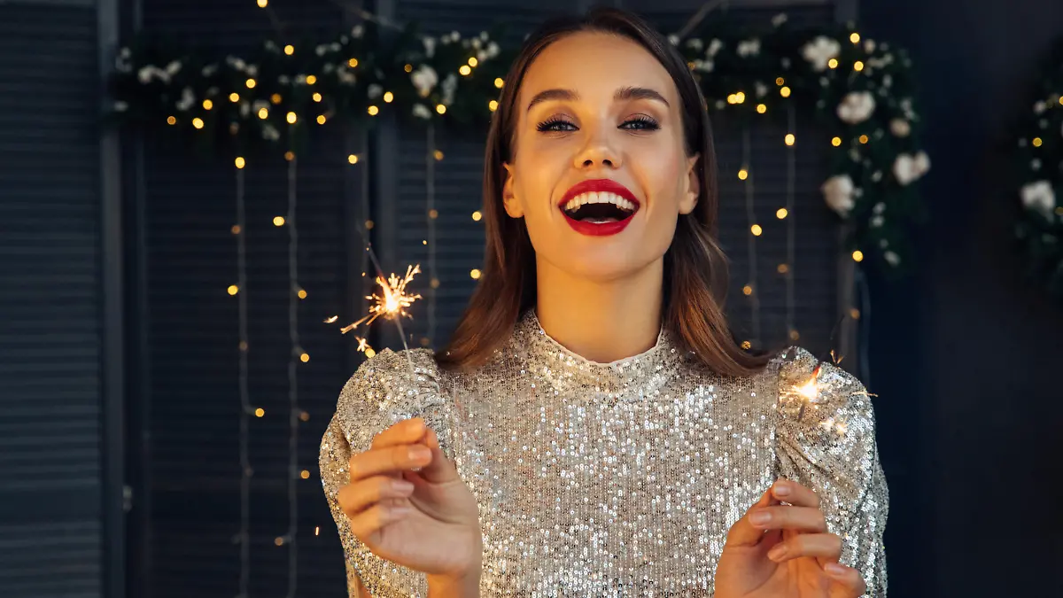 Happy beautiful woman holding festive sparkler among Christmas night
