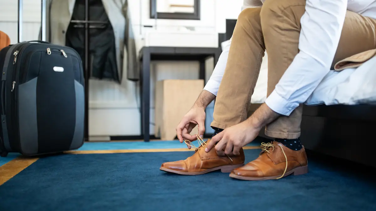 Cropped shot of man removing his shoe sitting on hotel bed. Businessman takes off his shoe in hotel room.