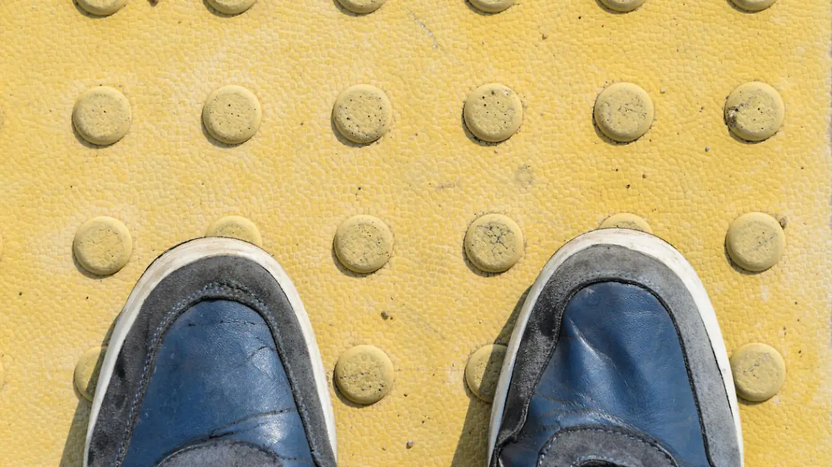 View from the First Person to his Feet, Standing in Front of the Sidewalk with Tactile Tiles to Navigate Blind People. Blue Sneakers on Yellow Tactile Paving Slabs.