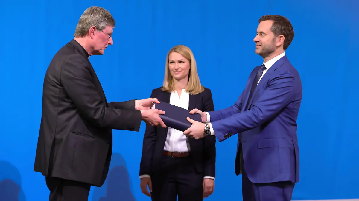18.03.2021, Nordrhein-Westfalen, Köln: Rechtsanwältin Kerstin Stirner (M) schaut zu, wie der von der Kirche beauftragte Anwalt Björn Gercke (r) dem Kölner Erzbischof Rainer Maria Woelki (l) während einer Pressekonferenz ein Exemplar eines Gutachtens zum Umgang des Erzbistums Köln mit sexuellem Missbrauch übergibt. Die Aufarbeitung des Umgangs mit sexuellem Missbrauch im Erzbistum Köln hat nach Angaben der katholischen Kirche rund 2,8 Millionen Euro gekostet. Darin enthalten seien zwei juristische Gutachten. Foto: Ina Fassbender/AFP Pool/dpa +++ dpa-Bildfunk +++