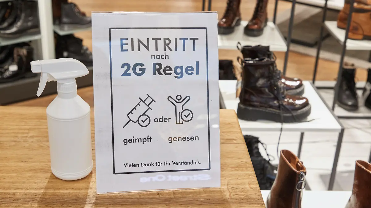 04.12.2021, Schleswig-Holstein, Norderstedt: Ein Hinweisschild mit der Aufschrift ·Eintritt nach 2G Regel geimpft oder genesen. Vielen Dank für Ihr Verständnis· steht auf einem Tisch am Eingang eines Schuhgeschäfts. Die Ausweitung der 2G-Regel auf den Einzelhandel ist in Schleswig-Holstein in Kraft getreten. Ungeimpfte können somit nur noch in Geschäften des täglichen Bedarfs einkaufen. Foto: Georg Wendt/dpa +++ dpa-Bildfunk +++