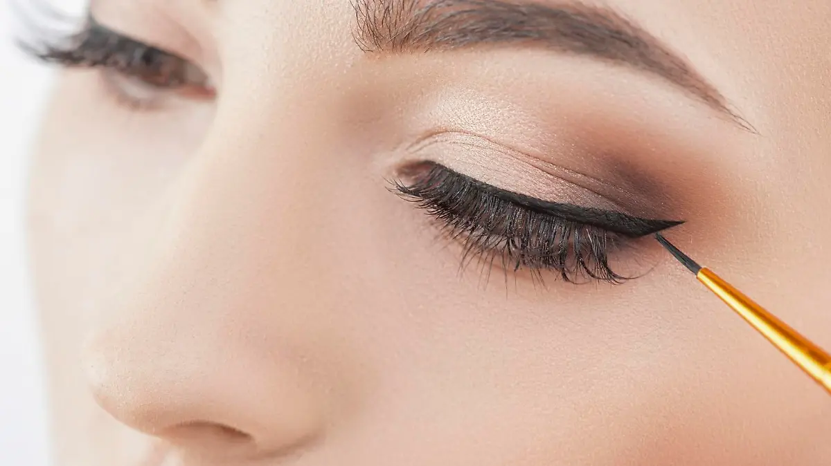 Close up of female eyes. The young woman is applying the eyeliner on her eye