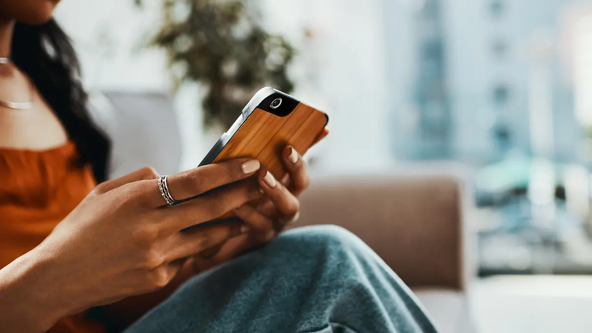 Cropped shot of a woman using a smartphone while relaxing on the sofa at home