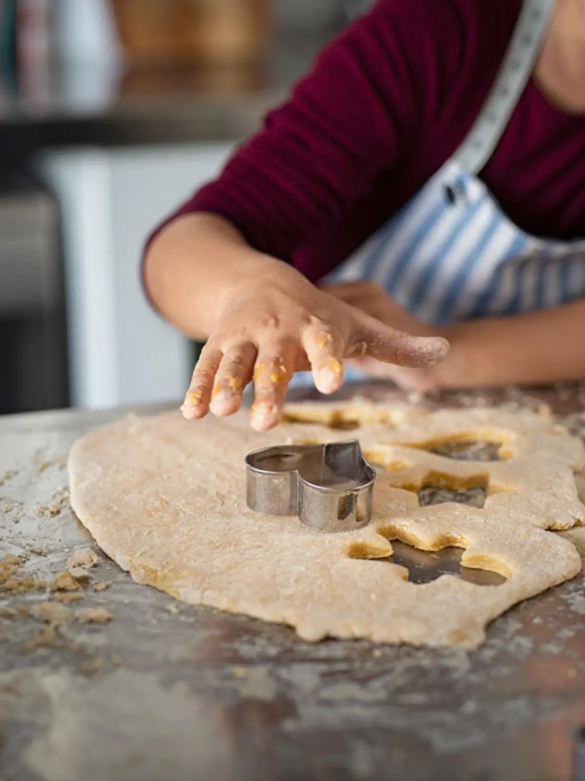 Closeup of child hands cutting cookies from dough. Little girl in apron pressing cookie cutter for shaping dough. Girl baking heart shaped christmas biscuits in the kitchen.