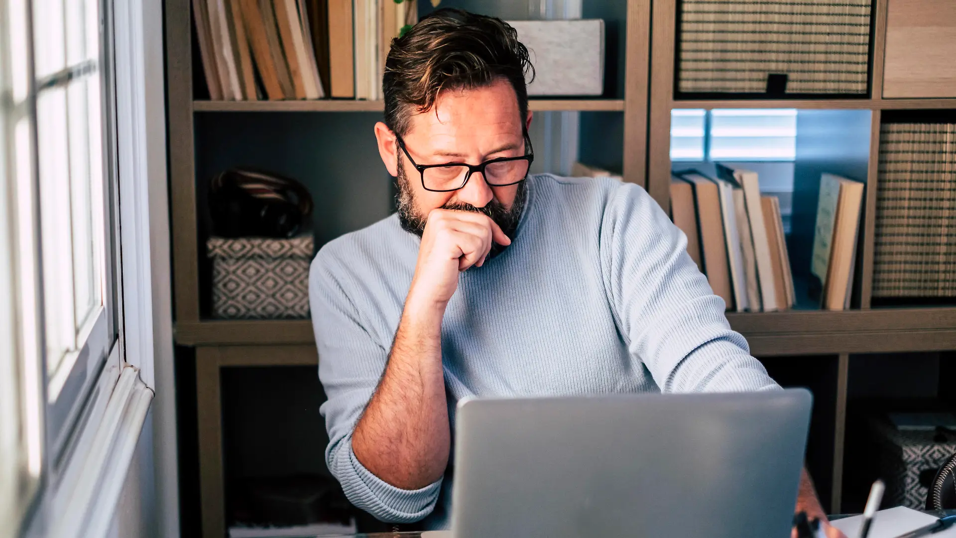 Male professional with hand on chin working on laptop at home model released Symbolfoto property released SIPF02497