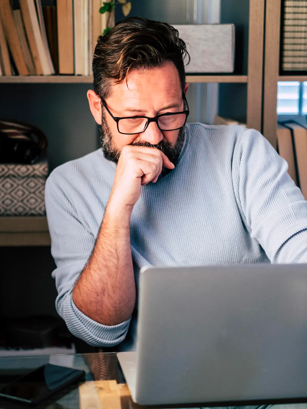 Male professional with hand on chin working on laptop at home model released Symbolfoto property released SIPF02497 