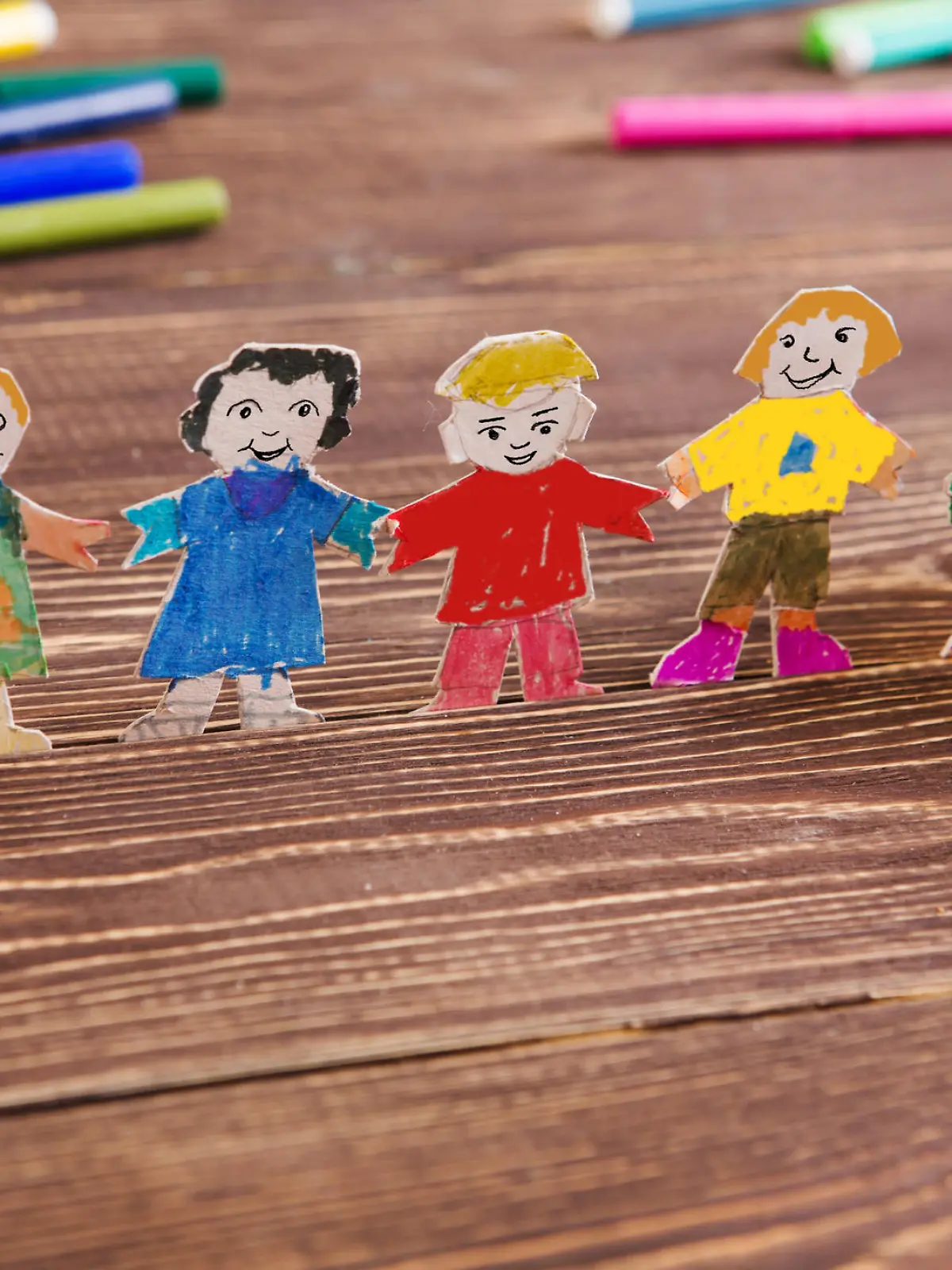 the child does figures of people of paper. Paper people on wooden background. Creative child play with craft.