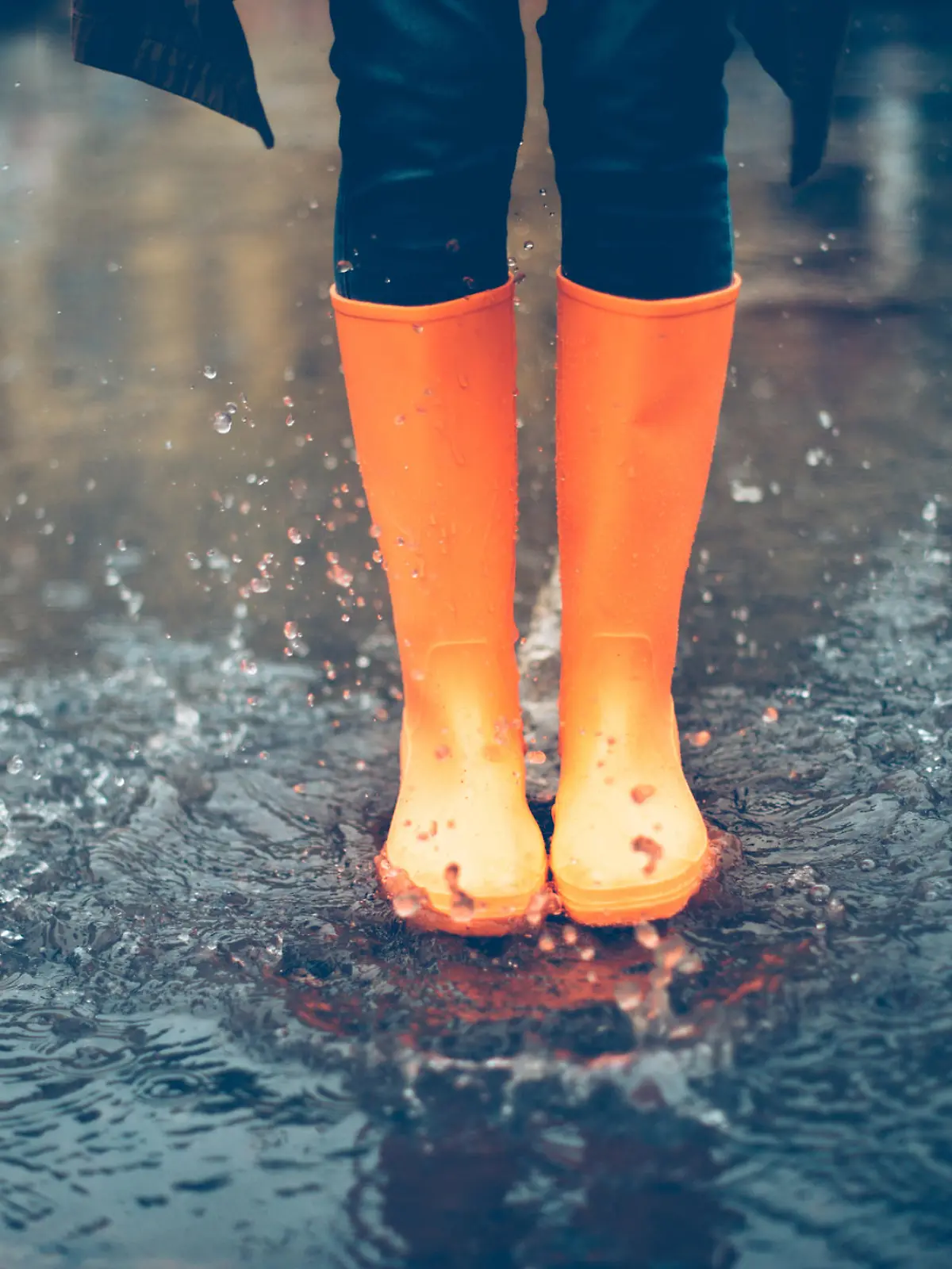 Close-up of woman in orange rubber boots jumping on the puddle