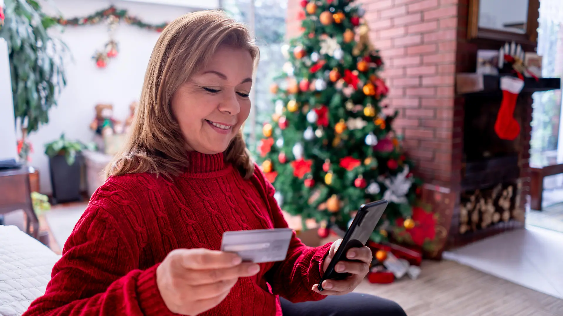 Beautiful mature woman relaxing on the couch shopping for christmas presents online using her smartphone and credit card - Consumerism concepts
