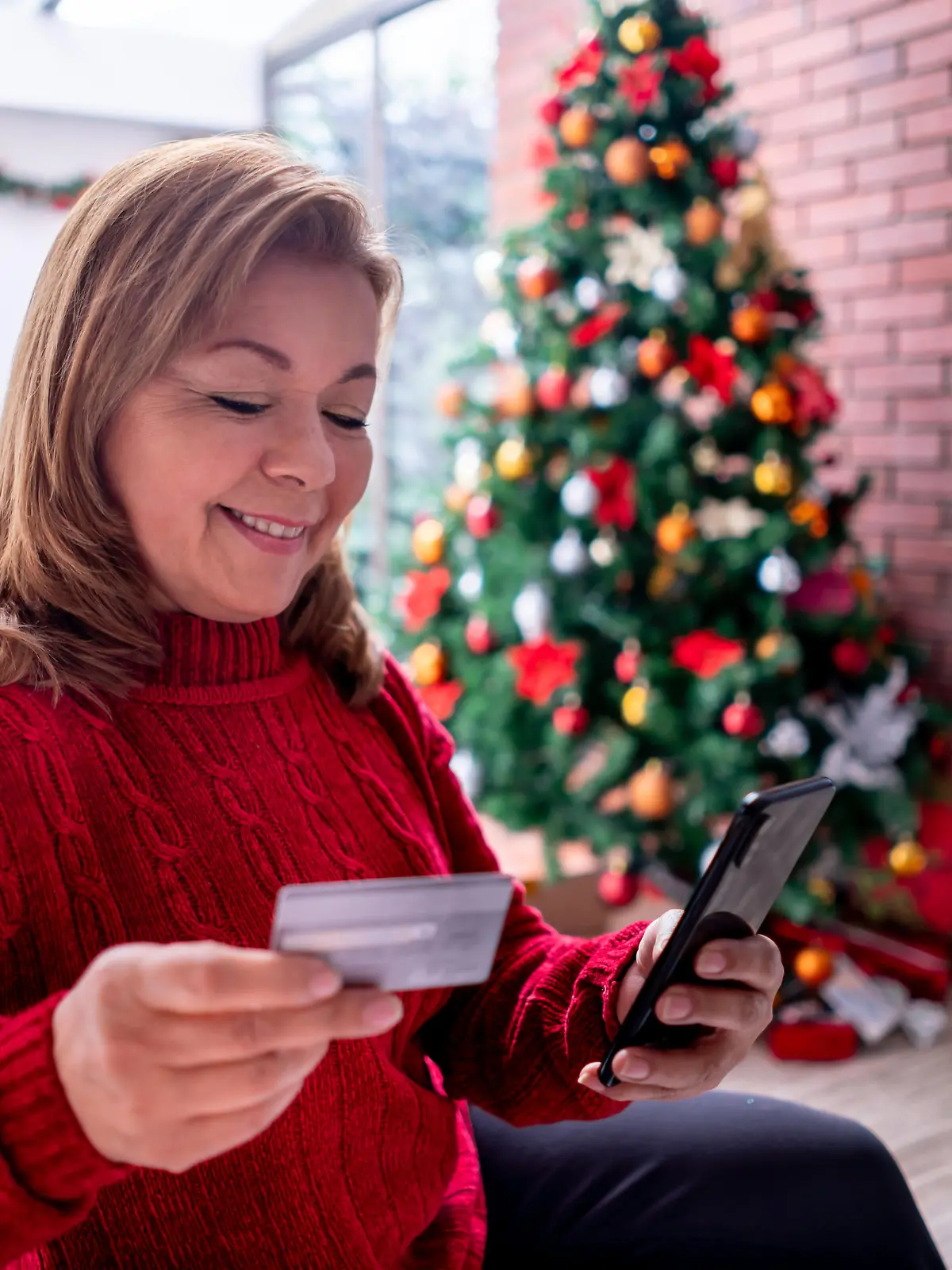 Beautiful mature woman relaxing on the couch shopping for christmas presents online using her smartphone and credit card - Consumerism concepts
