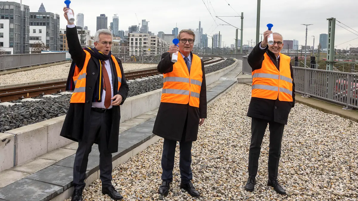 29.11.2021, Hessen, Frankfurt/Main: Zur Inbetriebnahme des neuen Gleises am Homburger Damm vor dem Frankfurter Hauptbahnhof lassen Hessens Verkehrsminister Tarek Al-Wazir (r-l - Bündnis 90/Die Grünen), Bahn-Vorstand Ronald Pofalla und Frankfurts Oberbürgermeister Peter Feldmann (SPD) ihre Pressluftröten erklingen. Nach vierjähriger Bauzeit ist das zusätzliche Streckengleis für Zufahrten zum Frankfurter Hauptbahnhof in Betrieb genommen worden. Mit dem etwa 800 Meter langen Gleis wird ein «Nadelöhr» im Frankfurter Gleissystem beseitigt. Foto: Helmut Fricke/dpa +++ dpa-Bildfunk +++