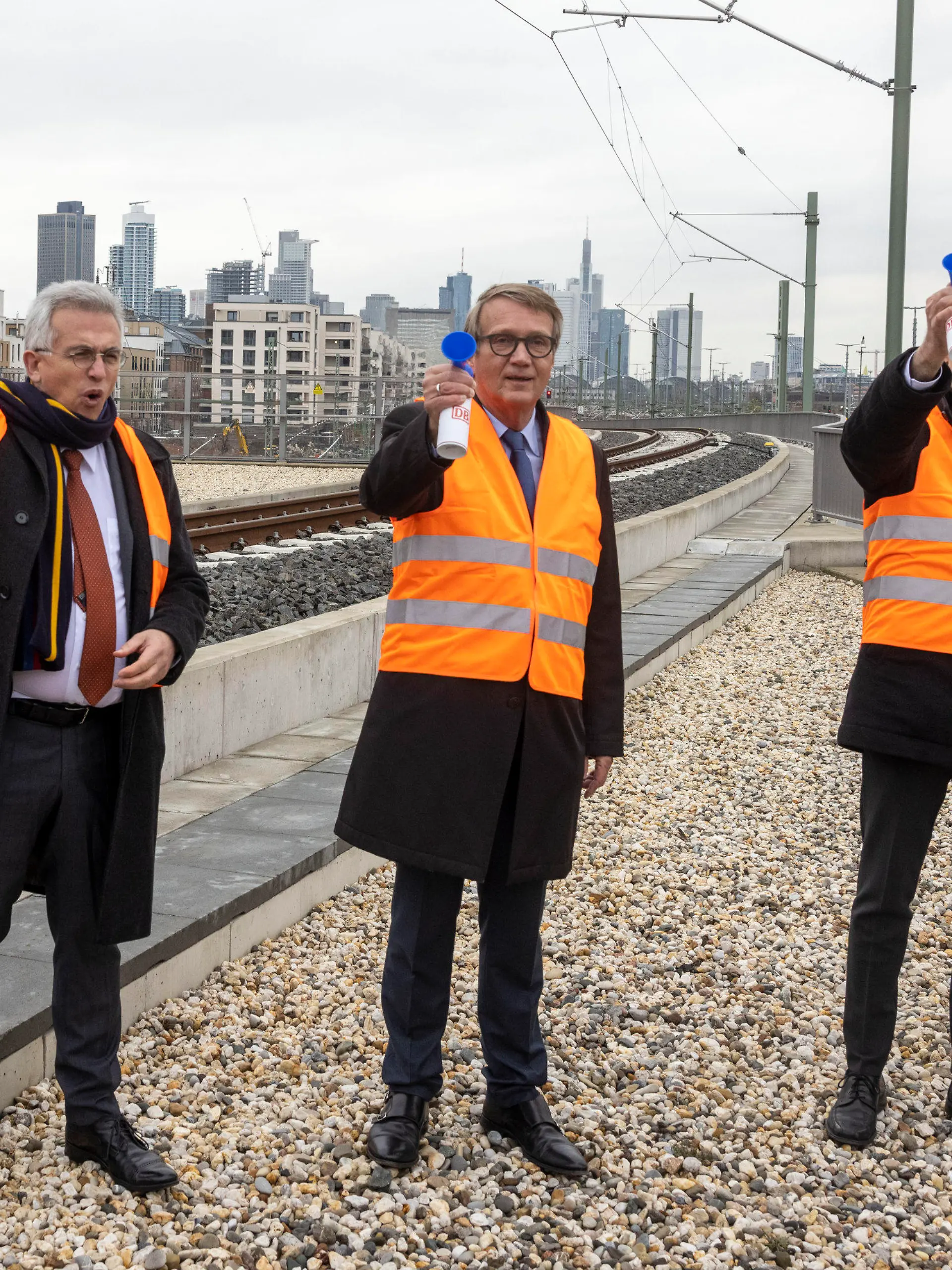 29.11.2021, Hessen, Frankfurt/Main: Zur Inbetriebnahme des neuen Gleises am Homburger Damm vor dem Frankfurter Hauptbahnhof lassen Hessens Verkehrsminister Tarek Al-Wazir (r-l - Bündnis 90/Die Grünen), Bahn-Vorstand Ronald Pofalla und Frankfurts Oberbürgermeister Peter Feldmann (SPD) ihre Pressluftröten erklingen. Nach vierjähriger Bauzeit ist das zusätzliche Streckengleis für Zufahrten zum Frankfurter Hauptbahnhof in Betrieb genommen worden. Mit dem etwa 800 Meter langen Gleis wird ein «Nadelöhr» im Frankfurter Gleissystem beseitigt. Foto: Helmut Fricke/dpa +++ dpa-Bildfunk +++