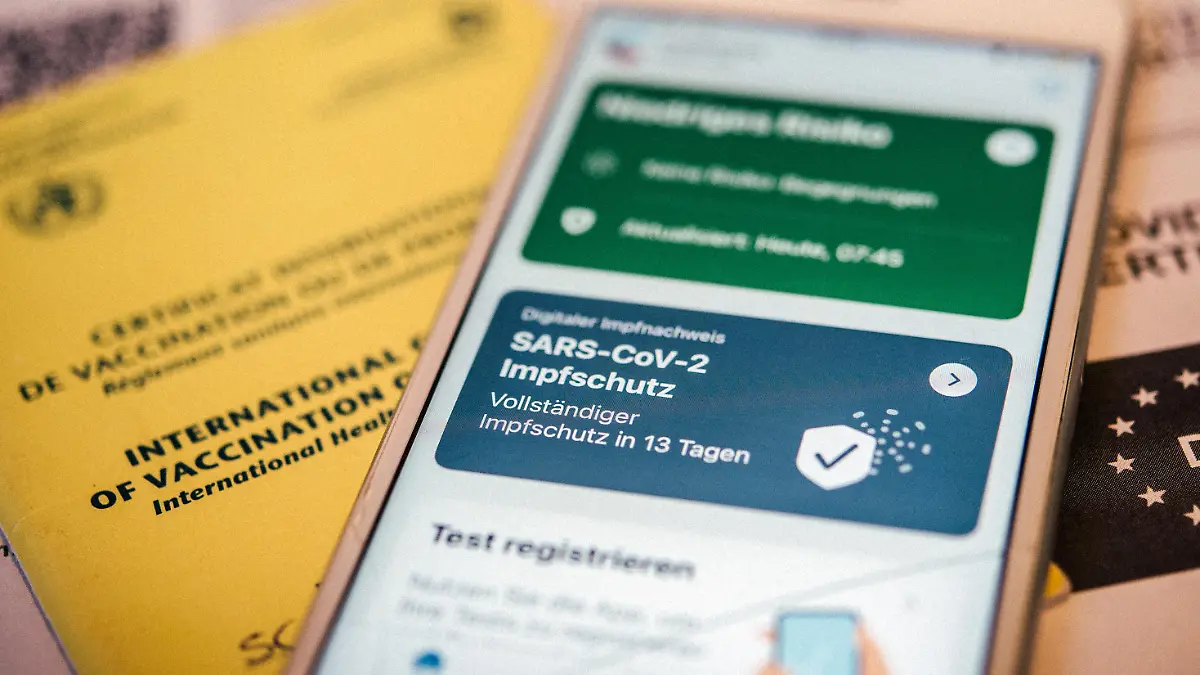 Ein gelber Impfausweis sowie der digitale Impfpass in der Corona-Warn-App liegen am 14.06.2021 in Berlin auf einem Tisch (gestellte Szene)