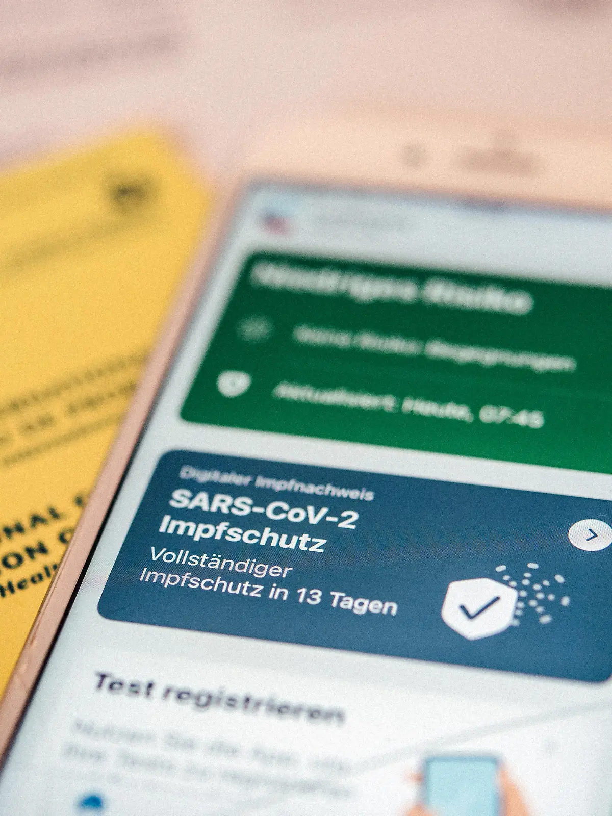 Ein gelber Impfausweis sowie der digitale Impfpass in der Corona-Warn-App liegen am 14.06.2021 in Berlin auf einem Tisch (gestellte Szene)