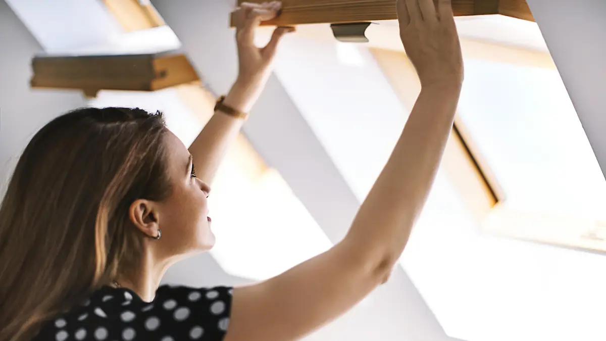 Beautiful brunette woman opening a skylight window. Side view. Horizontal.
