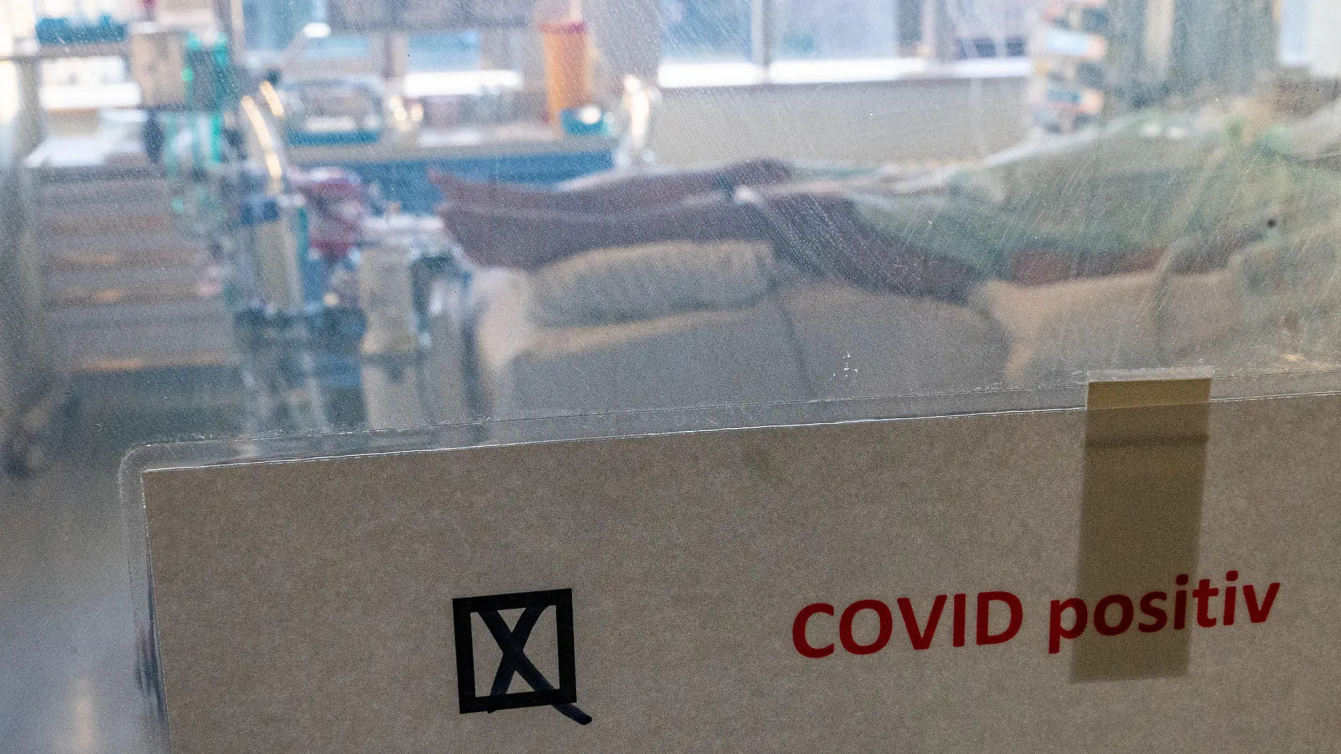 22.11.2021, Sachsen-Anhalt, Halle (Saale): Ein schwer an Covid-19 erkrankter Patient liegt hinter einem Schild mit dem Hinweis ·Covid positiv· in einem Isolierzimmer auf der Corona-Intensivstation im Universitätsklinikum in Halle/Saale. Das Krankenhaus ist ein Zentrum der Behandlung von Covid-19-Patienten in der Region. (Zu dpa "«Es ist grausam» - Schwerstarbeit auf Corona-Intensivstation") Foto: Hendrik Schmidt/dpa-Zentralbild/dpa +++ dpa-Bildfunk +++