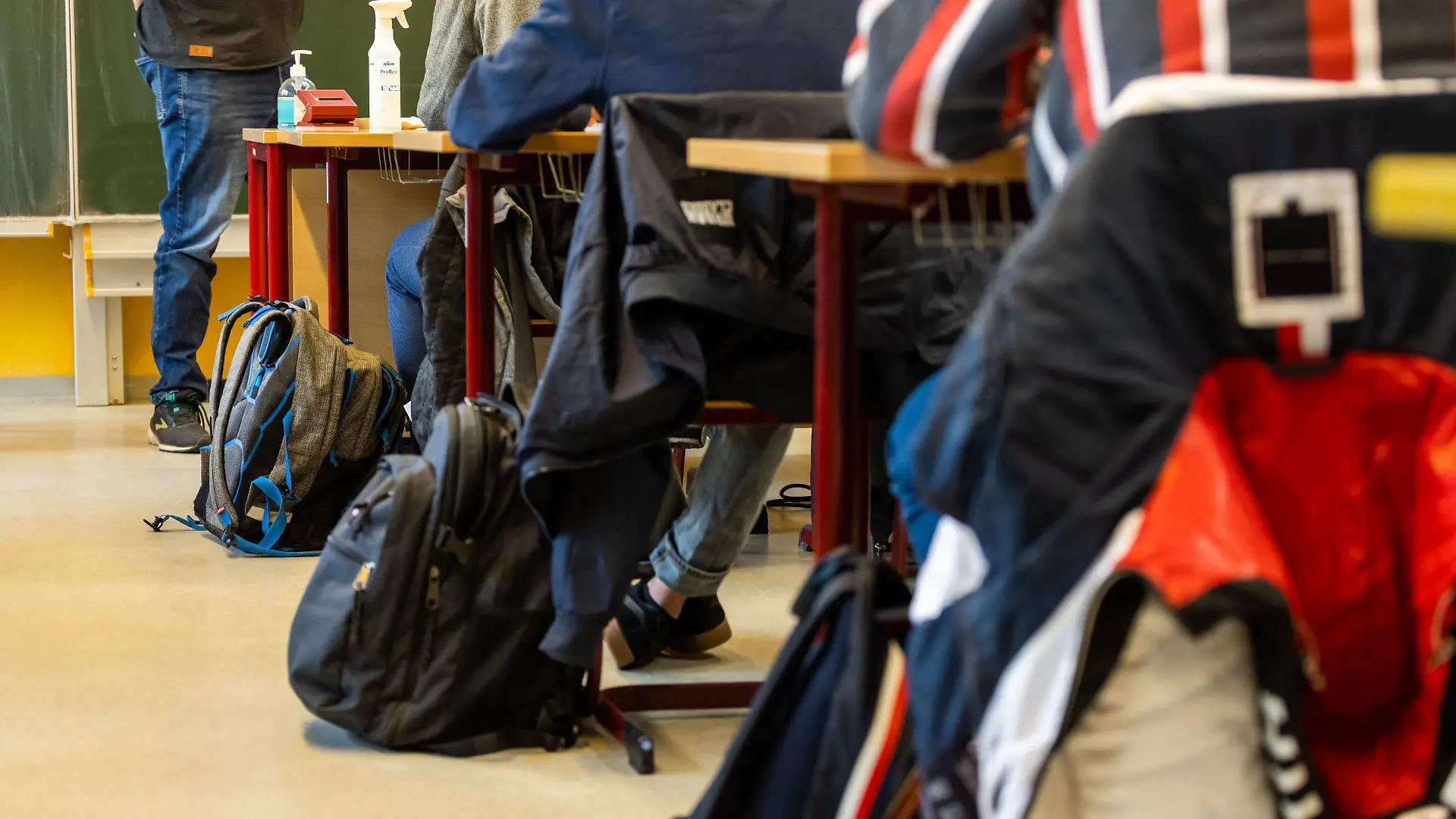 07.06.2021, Baden-Württemberg, Heitersheim: Rucksäcke stehen neben den Tischen, an denen die Schülerinnen und Schüler am Montagmorgen beim Unterricht in ihrer Klasse sitzen, während ein Lehrer vor der Tafel steht. Sie sind zum ersten Schultag nach den Pfingsferien zurück in der Johanniter-Realschule. Nach fast einem halben Jahr Home Schooling können Hunderttausende Schülerinnen und Schüler im Südwesten wieder ins Klassenzimmer zurück. Grund sind die sinkenden Corona-Inzidenzzahlen und die Impfung fast aller Lehrkräfte. Foto: Philipp von Ditfurth/dpa +++ dpa-Bildfunk +++