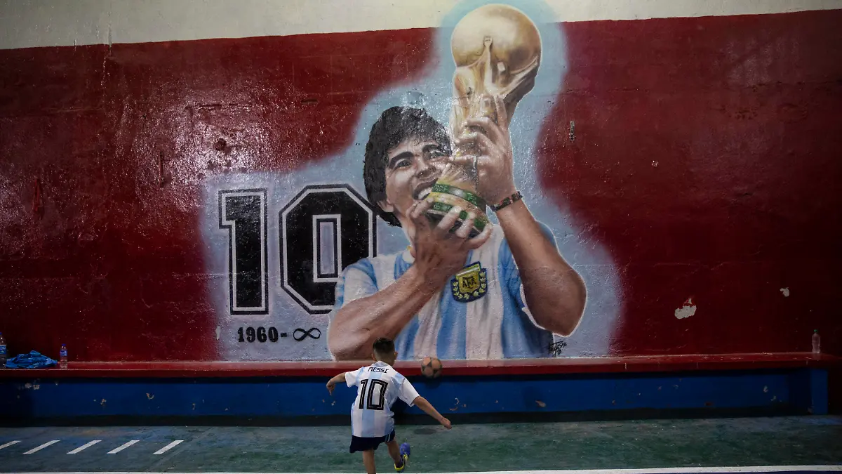 24.11.2021, Argentinien, Buenos Aires: Ein Junge kickt einen Fußball gegen eine Wand mit einem Wandgemälde des verstorbenen Fußballstars Diego Maradona im Club "Juventud Unida". Der erste Todestag der Fußballlegende jährt sich am 25. November. Foto: Rodrigo Abd/AP/dpa +++ dpa-Bildfunk +++
