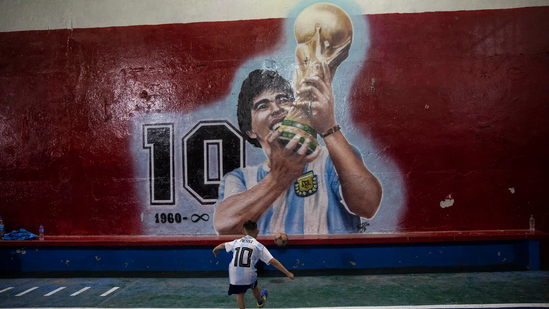 24.11.2021, Argentinien, Buenos Aires: Ein Junge kickt einen Fußball gegen eine Wand mit einem Wandgemälde des verstorbenen Fußballstars Diego Maradona im Club "Juventud Unida". Der erste Todestag der Fußballlegende jährt sich am 25. November. Foto: Rodrigo Abd/AP/dpa +++ dpa-Bildfunk +++
