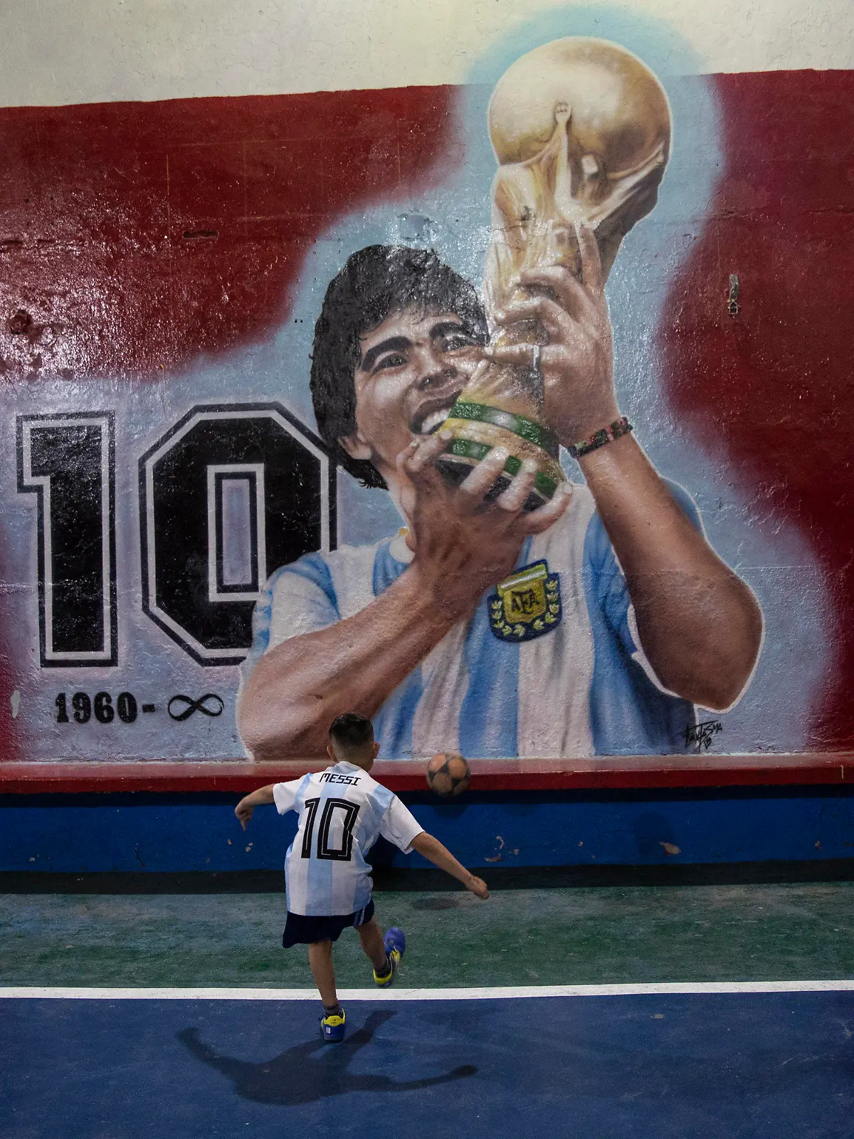 24.11.2021, Argentinien, Buenos Aires: Ein Junge kickt einen Fußball gegen eine Wand mit einem Wandgemälde des verstorbenen Fußballstars Diego Maradona im Club "Juventud Unida". Der erste Todestag der Fußballlegende jährt sich am 25. November. Foto: Rodrigo Abd/AP/dpa +++ dpa-Bildfunk +++