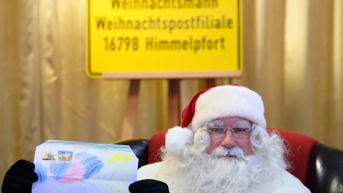 11.11.2021, Brandenburg, Fürstenberg/Havel/Ot Himmelpfort: Der Weihnachtsmann sitzt nach der Ankunft im Weihnachtspostamt in seinem Sessel und hält einen per Brief eingetroffenen Wunschzettel. Der Weihnachtsmann will sich an den Wochenenden bis Heiligabend jeweils von Freitag bis Sonntag in seinem Weihnachtspostbüro aufhalten. In dieser Zeit kann er durch das Fenster beim Beantworten der Post beobachtet werden. Aufgrund der weiterhin anhaltenden Corona-Infektionsgefahr ist sein weihnachtlich geschmücktes Büro jedoch für Besucher in diesem Jahr nicht öffentlich zugänglich. Foto: Soeren Stache/dpa +++ dpa-Bildfunk +++