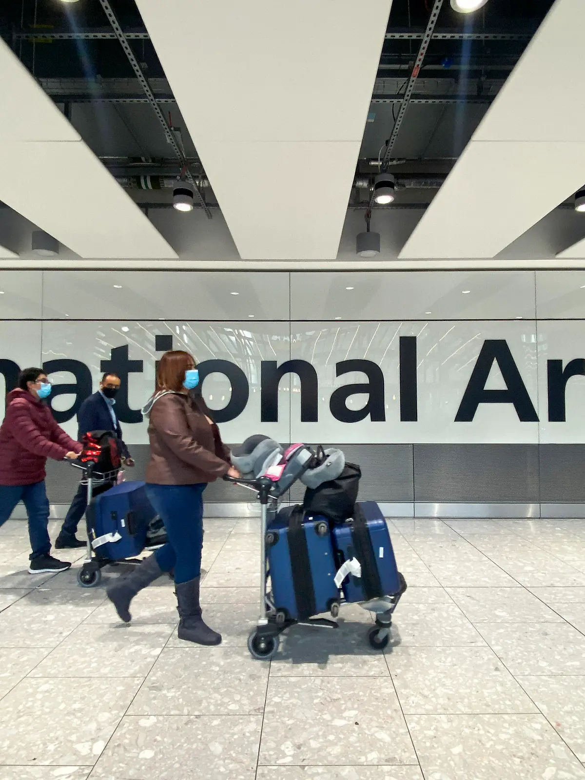 26.11.2021, Großbritannien, London Heathrow: Passagiere gehen mit ihrem Gepäck durch das Ankunftsterminal auf dem Londoner Flughafen Heathrow. Nach der Entdeckung einer neuen Virusvariante gab die Regierung von Großbritannien bekannt, dass es ein Flugverbot für Flüge aus Südafrika und fünf anderen Ländern des südlichen Afrikas verhängt hat und dass alle Personen einen Corona-Test durchführen müssen, die kürzlich aus diesen Ländern eingereist sind. Foto: Alberto Pezzali/AP/dpa +++ dpa-Bildfunk +++