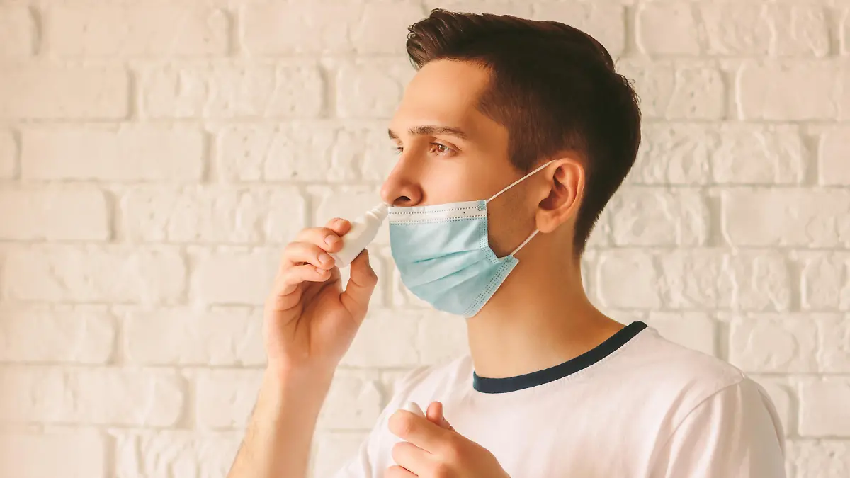 Portrait of young sick man using nasal drops for runny congested nose. Confident sick doctor in medical protective mask on face using nose spray. Pandemic coronavirus COVID-19 nCov-19 symptoms