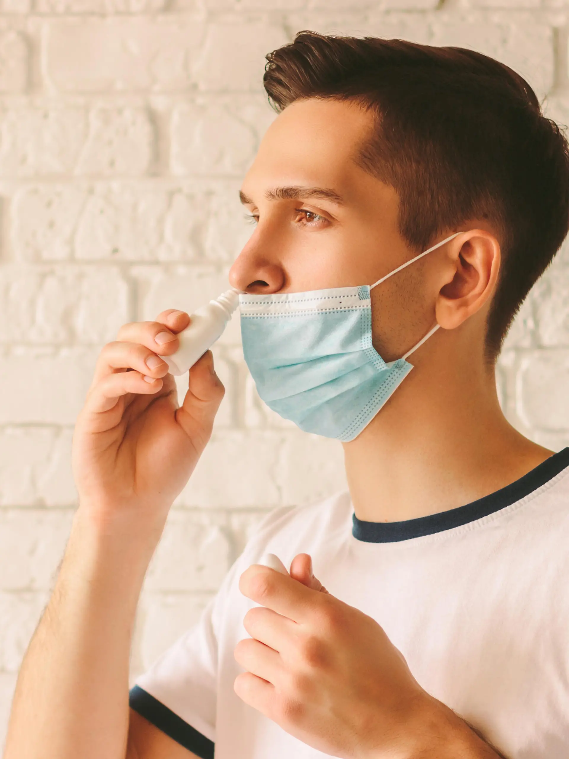 Portrait of young sick man using nasal drops for runny congested nose. Confident sick doctor in medical protective mask on face using nose spray. Pandemic coronavirus COVID-19 nCov-19 symptoms