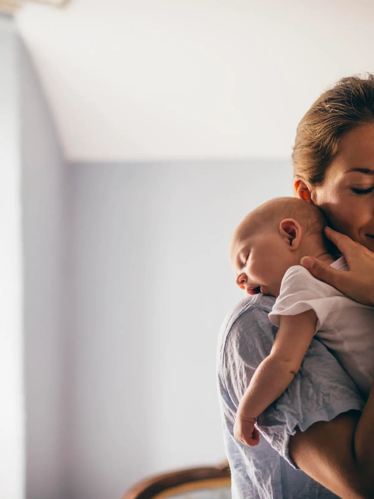 A happy new mother smiles as she craddles her sleeping baby in her arms. She has her eyes closed as she holds her close.