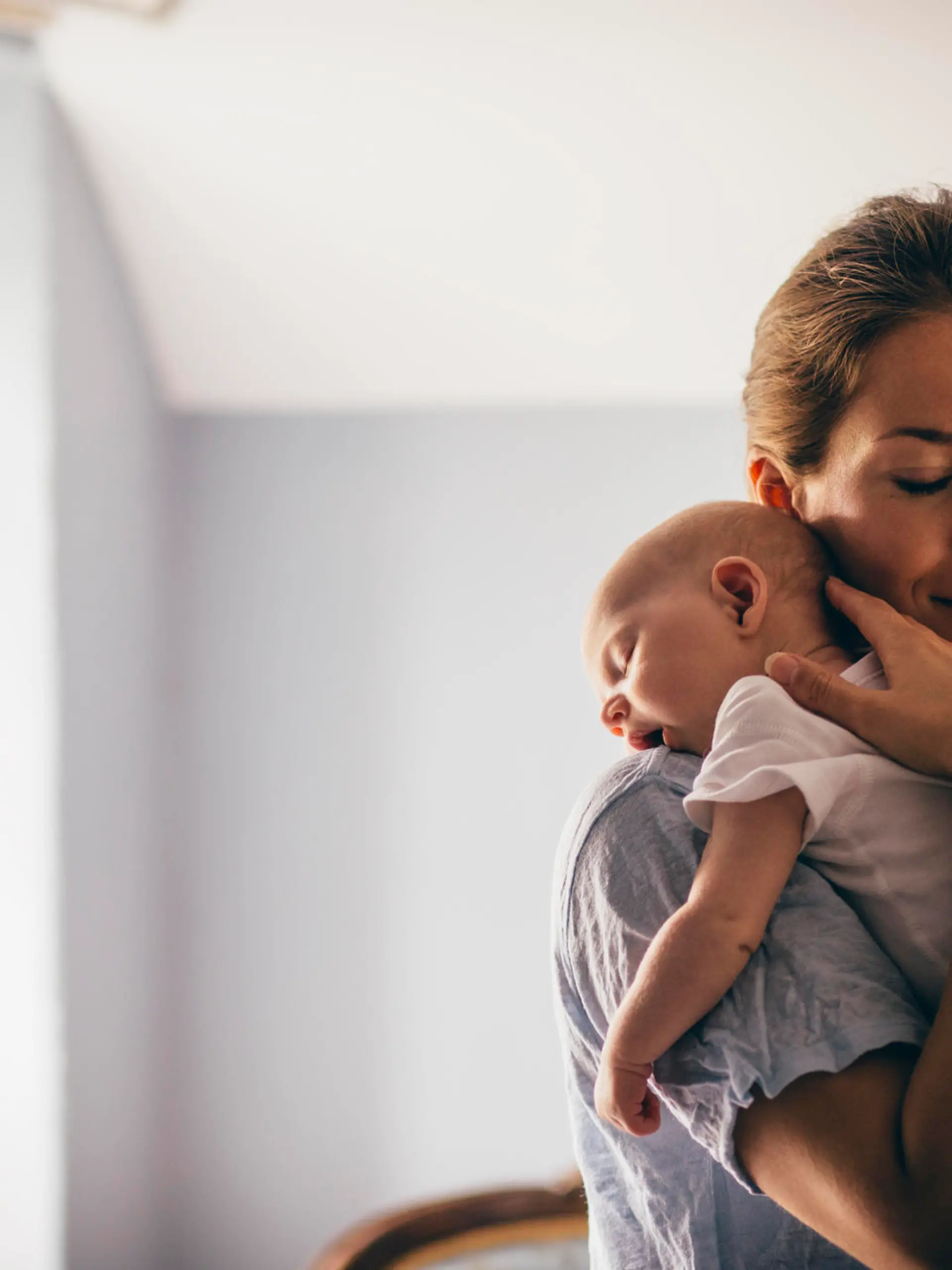 A happy new mother smiles as she craddles her sleeping baby in her arms. She has her eyes closed as she holds her close.
