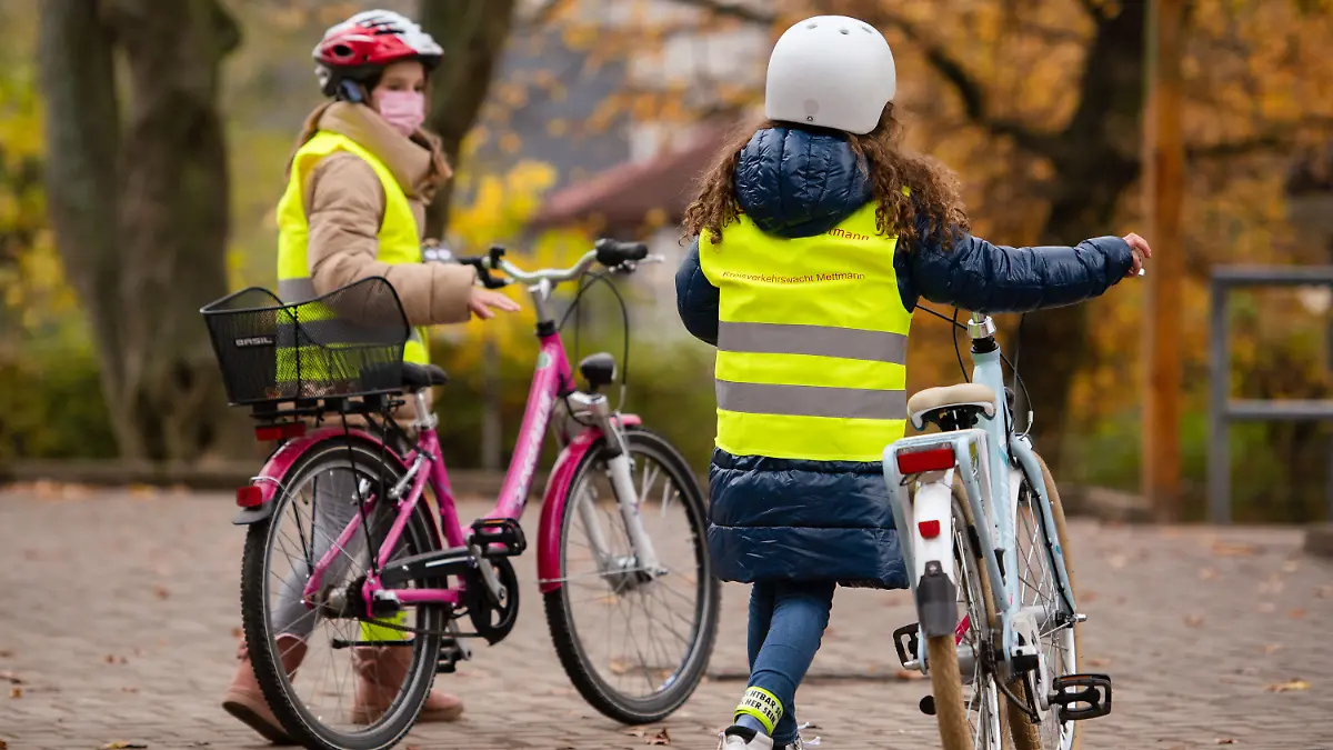 12.11.2021, Nordrhein-Westfalen, Erkrath: Kinder mit Warnwesten schieben nach einem Pressetermin ihre Fahrräder um den Schulhof. Um die Sichtbarkeit von Kindern auf dem Fahrrad zu verbessern, stellt das Land Nordrhein-Westfalen Speichenreflektoren für rund 36 000 Fahrräder zur Verfügung. Sie sollen in den kommenden Wochen an Kinder übergeben werden, die in diesem Jahr die Radfahrprüfung abgelegt haben. Foto: Marius Becker/dpa - ACHTUNG: Nur zur redaktionellen Verwendung und nur mit vollständiger Nennung des vorstehenden Credits +++ dpa-Bildfunk +++