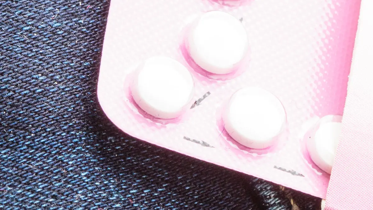 Healthcare medicine, contraception and birth control. Closeup oral contraceptive pills, red condom on denim pocket background