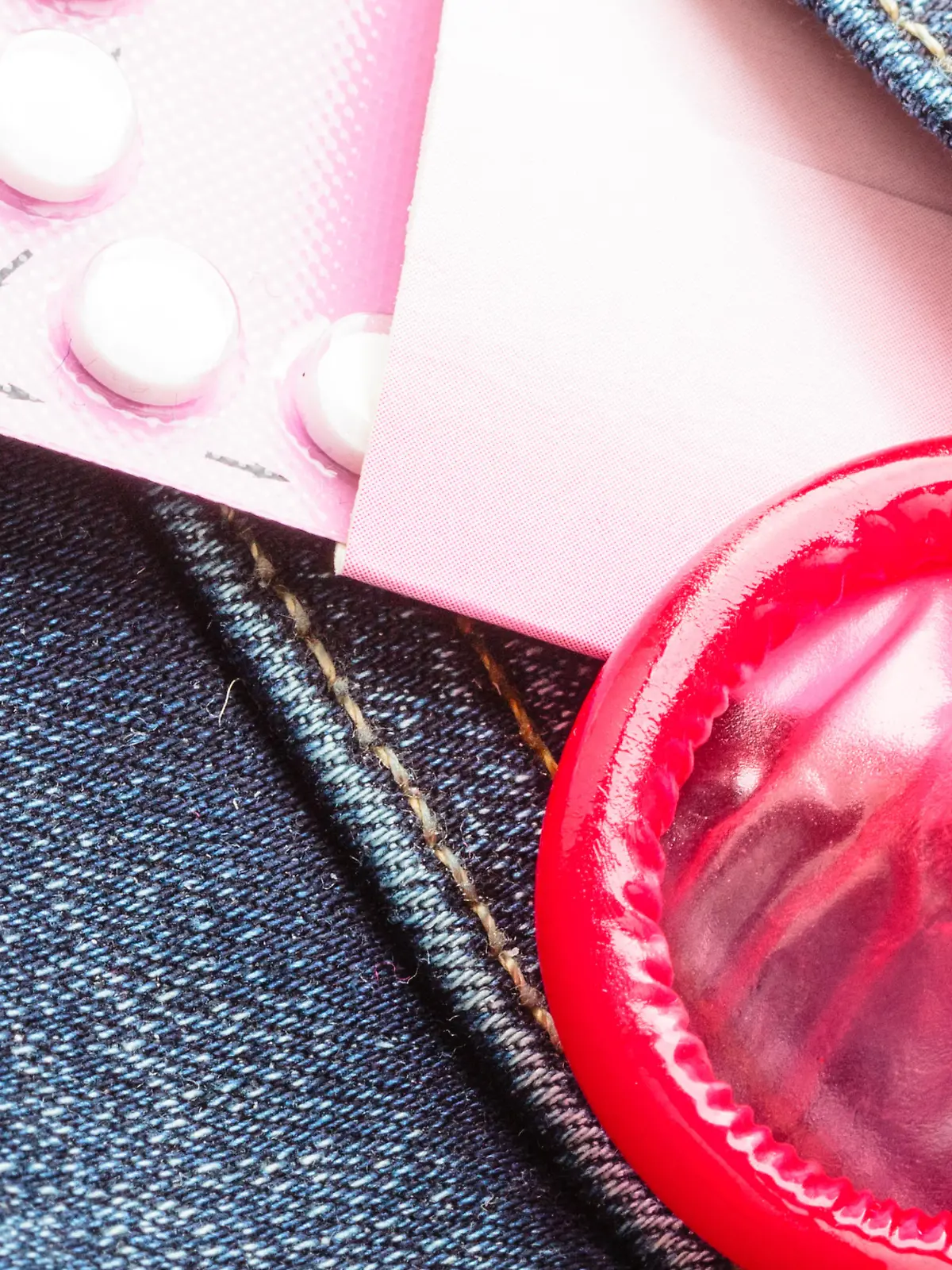 Healthcare medicine, contraception and birth control. Closeup oral contraceptive pills, red condom on denim pocket background