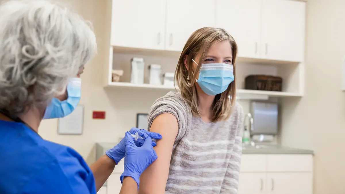 Woman is receiving a Covid-19 vaccination in doctor's office from senior nurse or doctor