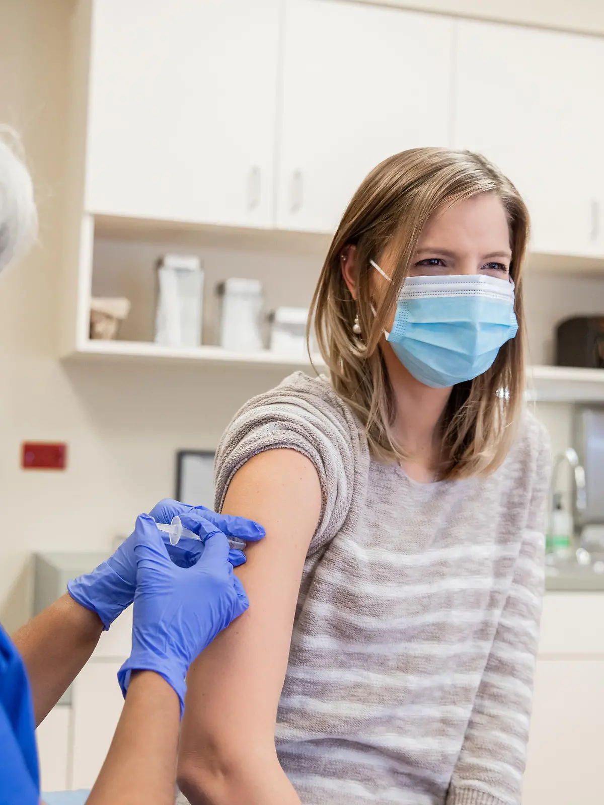 Woman is receiving a Covid-19 vaccination in doctor's office from senior nurse or doctor