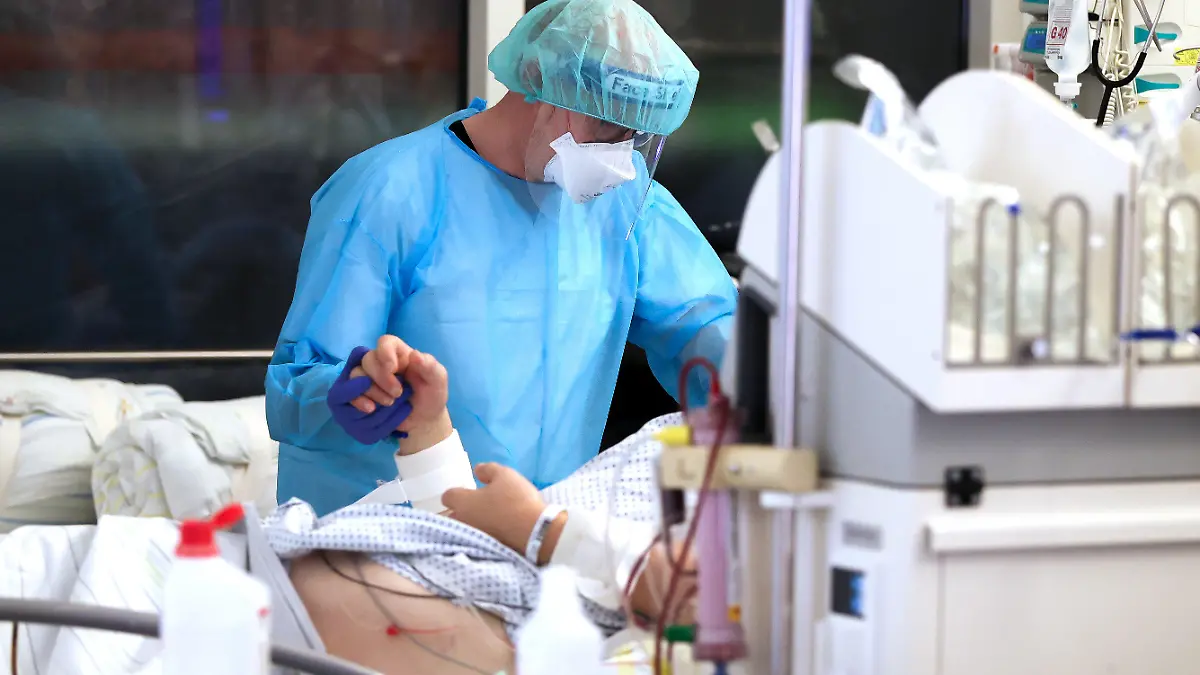 dpatopbilder - ARCHIV - 15.11.2021, Sachsen, Leipzig: Ein Facharzt versorgt einen Covid-19-Patienten auf der Intensivstation der Leipziger Uniklinik und hält dessen Hand. (zu dpa "Intensivmediziner: Corona-Lage sehr besorgniserregend") Foto: Jan Woitas/dpa-Zentralbild/dpa +++ dpa-Bildfunk +++